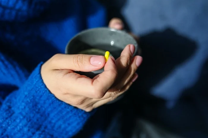 A person holding medication and tea during alcohol detox